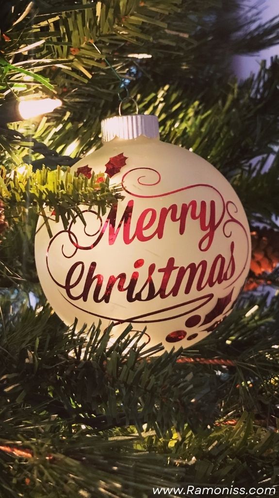 In the photo, the christmas ball is hanging on the christmas tree, and merry christmas is written on the christmas ball with a red stylish font.