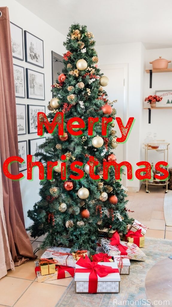 A white room has photo frames on the walls and a christmas tree decorated with christmas balls and mini toys, a flower pot in the cupboard, and a table in the room. Merry christmas is written in red font.