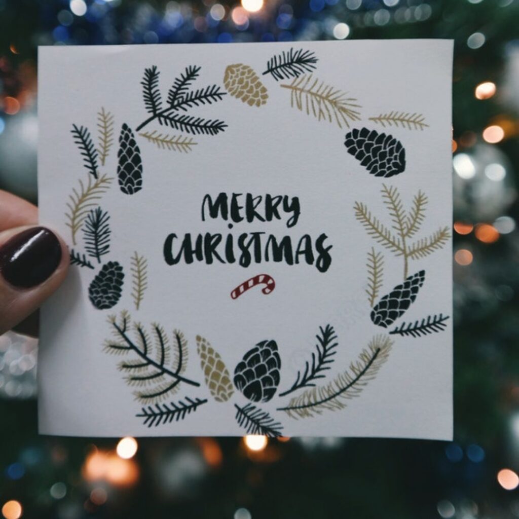 A woman is holding a merry christmas card with a beautiful background behind it.