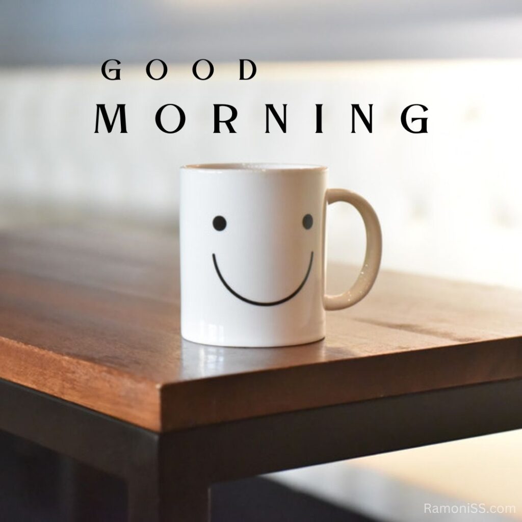 In the photo, ismaili emoji printed cup is placed on the wooden table and good morning is also written in the photo.