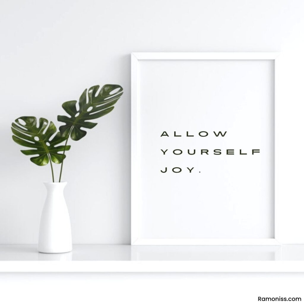 In the image, a white flowerpot white photo frame has kept on the white table, and motivational thoughts text that says allow yourself joy.