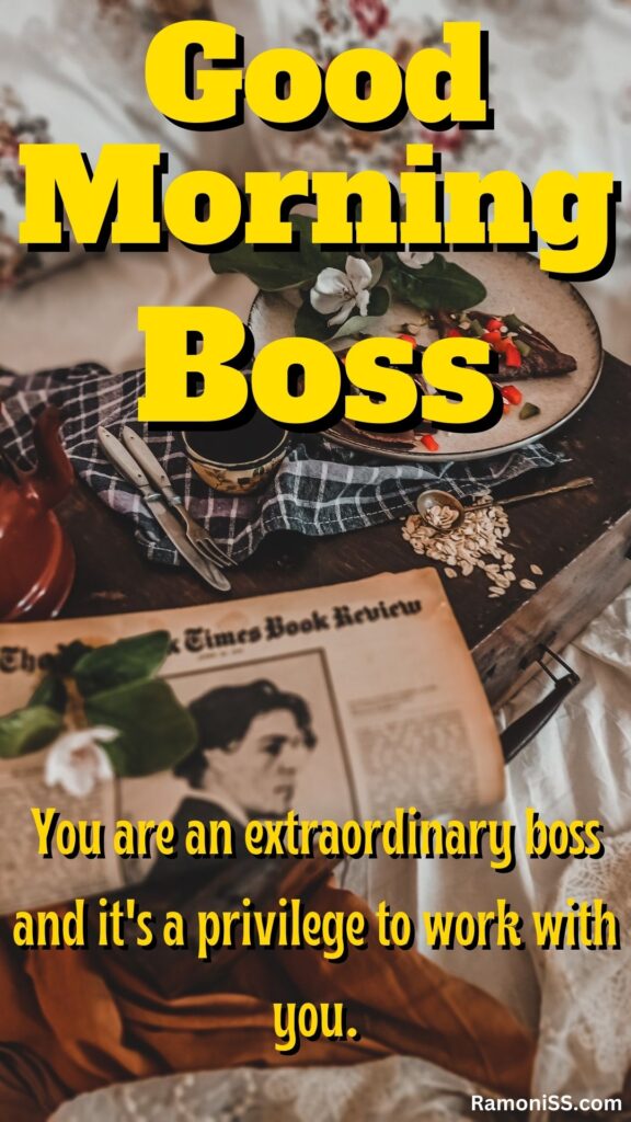 Good morning boss is written in the image and in the background image a plate with flowers, a cup full of black tea, a knife, a spoon a kettle, and a newspaper in the wooden tray placed on the white bed.