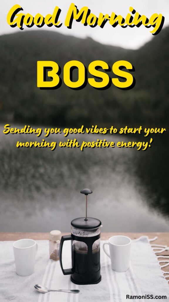 Good morning boss written in the image and in the background image a white colored cloth is spread on a table by the lake and a thermos of black coffee, a spoon, and a box of coffee powder are placed on the cloth.
