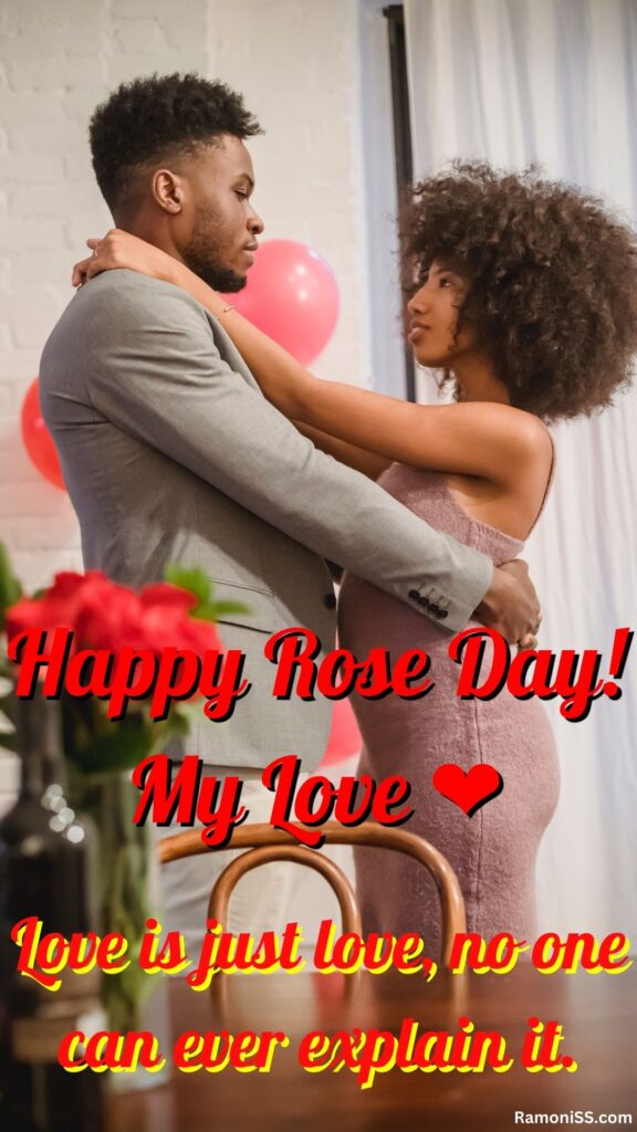 In the photo, the boyfriend and girlfriend are standing inside a room hugging each other, dressed in beautiful outfits, and wishing happy rose day, and a bouquet of roses is placed on the table.