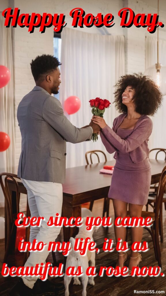 In the photo, the lover and the girlfriend are standing inside a room, which the lover is giving a rose to his girlfriend and wishing her a very happy rose day, and in the photo, there are white curtains on the window inside the room, and the table, chairs are also kept. .