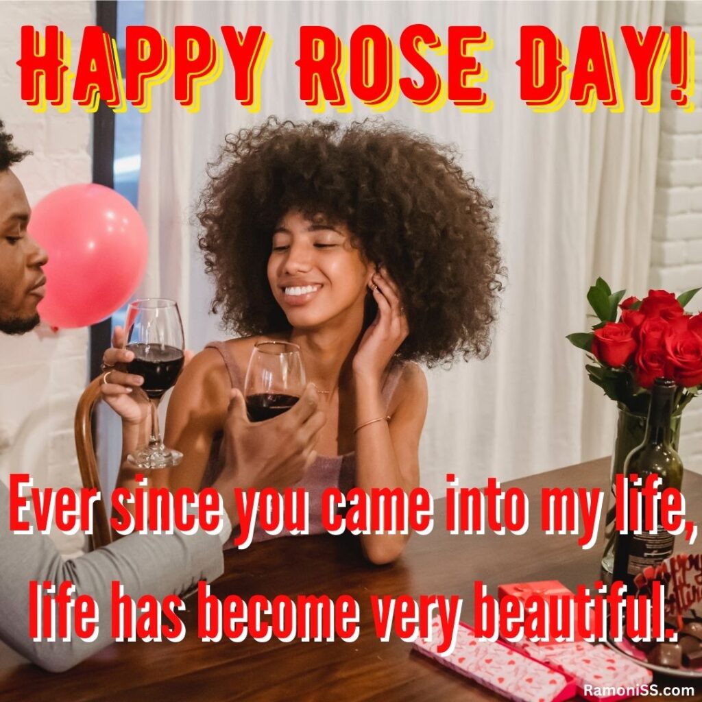Curly hair girl sitting with her boyfriend and celebrating rose day with drink. Roses placed on the wooden table.
