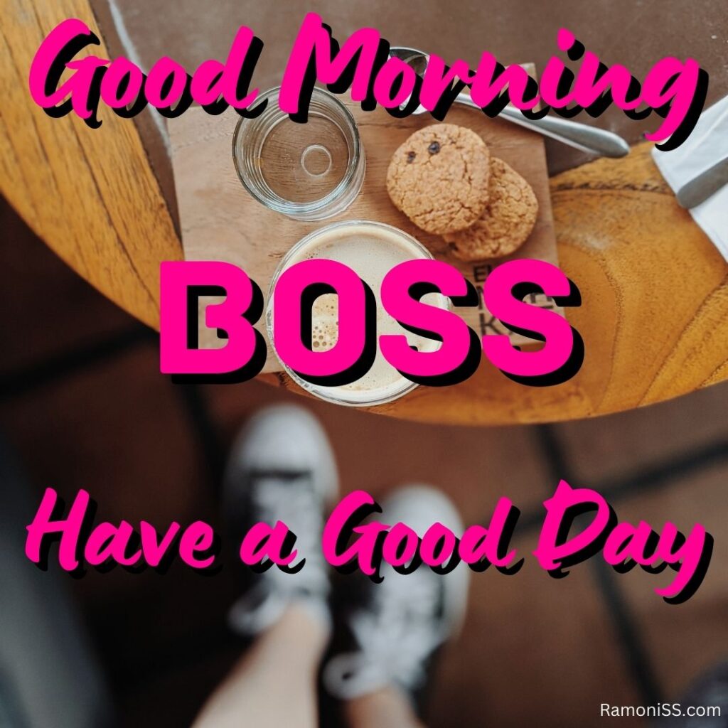 Good morning boss written in the image and in the background of the photo a cup of coffee, a glass of water, and two biscuits is placed on a wooden table.