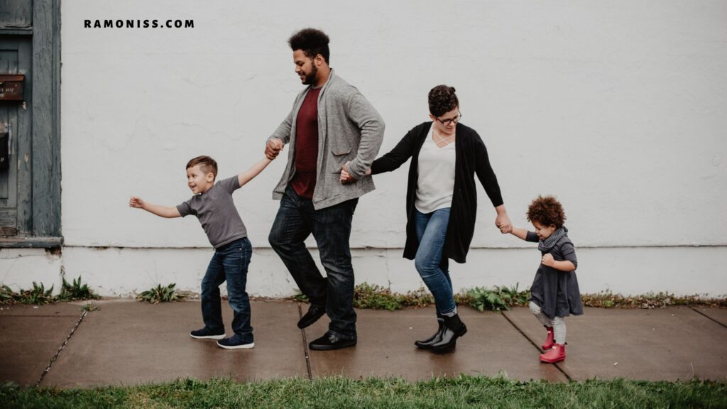 In the photo, happy parents and their two young children are walking on the sidewalk holding each other's hands.