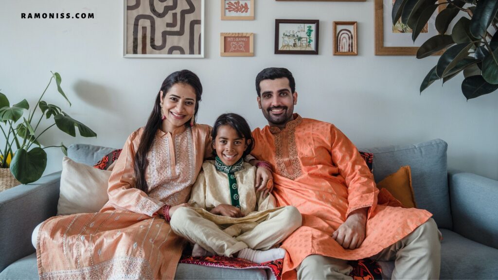 In the photo, happy parents are smiling while sitting on the sofa with their son indoors.