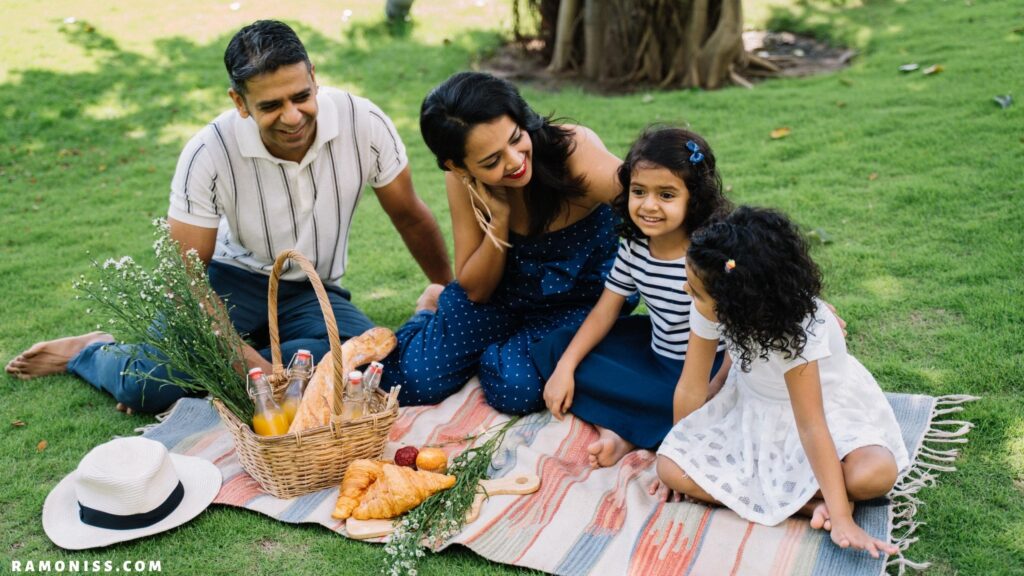 In the photo of a happy indian family, a mother and father with their two daughters are having a picnic in the garden.