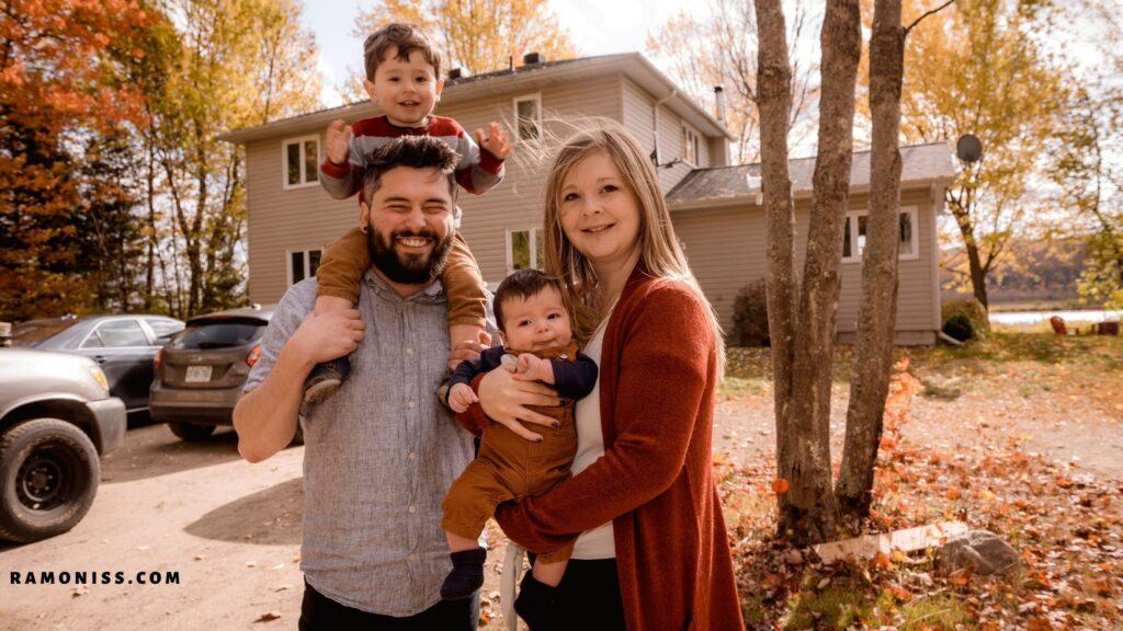 In the photo, the parents of two children are standing under the tree outside the house with the children in their arms.