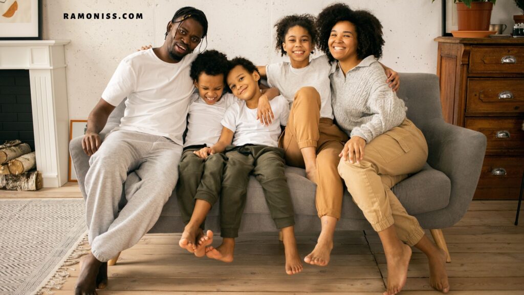 In the photo, two little boys and one of their sisters are sitting on a gray sofa with their parents at home