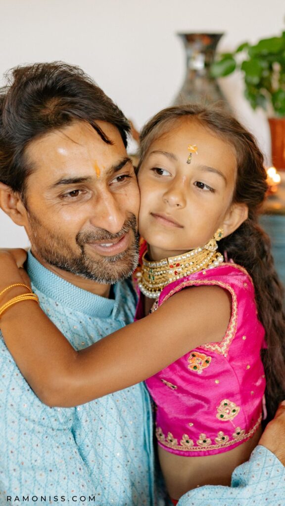 In the picture, an indian father is hugging his daughter, who looks very happy.