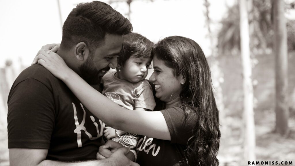 Black and white photo of happy mother and father with a small child in their arms, smiling at each other.