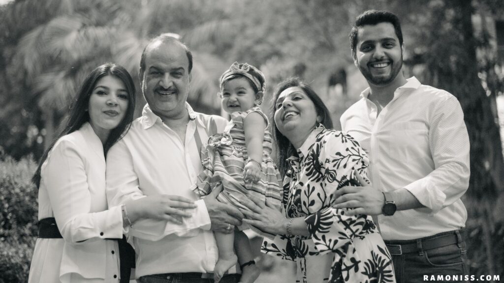 Happy full family black and white image, the photo shows a happy indian family of 5 members, a little girl in her grandfather's arms and the girl's parents and grandmother